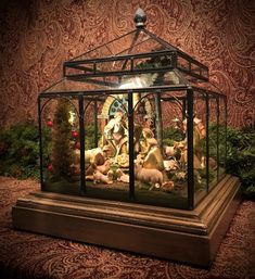 the nativity scene is in a glass box on top of a wooden stand with flowers and greenery