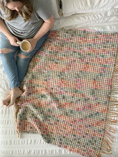 a woman sitting on top of a bed next to a blanket holding a coffee cup