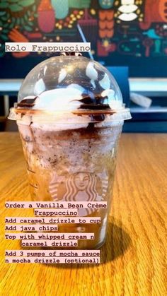 an iced coffee drink with whipped cream and chocolate toppings in a plastic cup on a wooden table