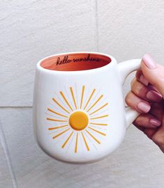 a person holding a coffee mug with the words hello sunshine on it in front of a white wall