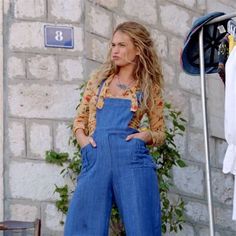 a woman in overalls standing next to a brick wall with her hands on her hips