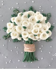 a bridal bouquet made out of white roses and green leaves on a gray surface