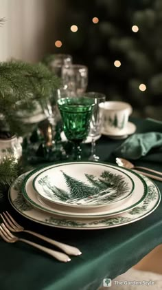 a table set for christmas with green and white plates, silverware and evergreen decorations