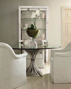 a glass table with chairs around it and a vase on the top, in front of two white chairs