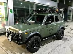 an army green truck parked in front of a building with luggage on the roof rack