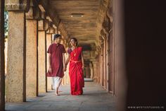 a man and woman are walking down the hall together in red sari dresses, holding hands