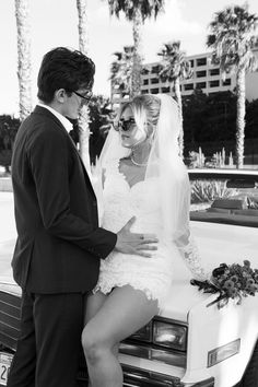 a man and woman standing next to each other in front of a car with palm trees