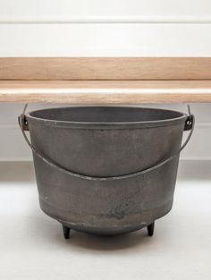 an old metal bucket sitting on top of a wooden table next to a bench with white walls