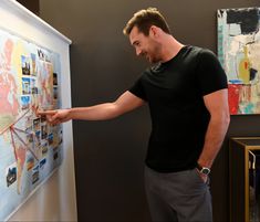 a man is pointing to a poster on the wall with his hand in it's pocket