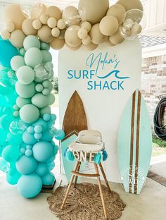 a surfboard and balloon arch is displayed in front of a sign that says happy surf shack