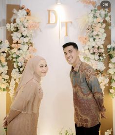 a man and woman standing next to each other in front of a floral display with flowers