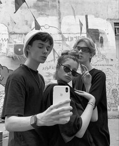 three people standing in front of a wall with graffiti on it and one person holding an iphone