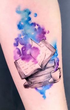 a watercolor tattoo with an open book on it's arm and stars in the background