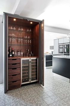 an open cabinet in the middle of a kitchen with wine glasses and bottles on it