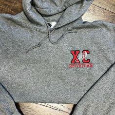 Elevate your training and race-day apparel with our premium hooded sweatshirt, featuring a detailed XC and track logo embroidered on the left chest. Personalize it with your team, coach, or player name to make a statement on and off the field. This sweatshirt blends functionality with team pride, offering the perfect combination of warmth and style for all cross country enthusiasts. Whether you're hitting the trails or cheering from the sidelines, this sweatshirt keeps you cozy and showcases you Cotton Hoodie With Embroidered Logo For Sports, Sports Hoodie With Embroidered Logo, College Fan Apparel Hoodie With Embroidered Logo, Gray Varsity Hoodie For Sports, Varsity Hoodie With Embroidered Logo For Sports Season, Collegiate Hoodie With Embroidered Logo For Sports, Sporty Fleece Hoodie With Embroidered Graphics, Embroidered Logo Hoodie For Sports Events, Sporty Hooded Sweatshirt With Embroidered Graphics