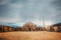 an old brick building sitting in the middle of a dirt field next to some buildings