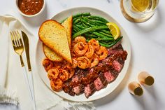 a plate with meat, shrimp, and green beans next to two glasses of beer