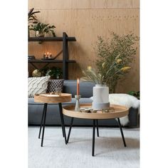 two wooden tables with candles on them in front of a gray couch and white rug