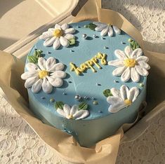 a blue cake decorated with white flowers and the words happy on it is in a box