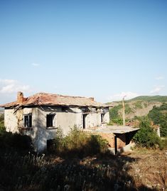 an old run down house sitting in the middle of a field next to a hill