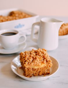 a piece of cake sitting on top of a white plate next to a cup of coffee