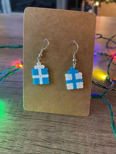 a pair of blue and white earrings on a table with christmas lights in the background