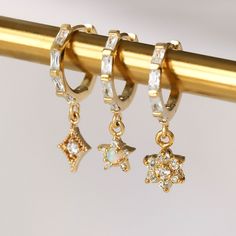 These gold dangle hoop earrings are set with cute flower charms and huggie hoop earrings. The charms and hoops shine beautifully and give you a statement look! Wear with other gold earrings to create your ear stack and enjoy mixing & matching. 18K gold plated huggie earrings 18K gold plated charms Sold individually or as a pair Earring size: 13 mm Charm size: 5.5 mm x 9.5 mm Cute Gold Earrings, Crystal Earrings Wedding, Ear Party, Dangle Hoop Earrings, Ear Stack, Synthetic Opal, Cute Flower, Solid Gold Jewelry, Huggie Earrings