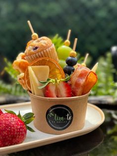 a cup filled with assorted fruit on top of a table next to strawberries