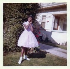 an old photo of a woman in a dress talking on a cell phone outside her house