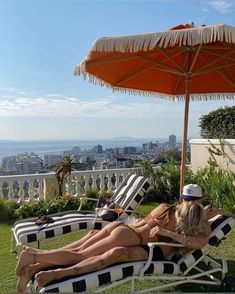 a woman laying on top of a lawn chair next to an orange and white umbrella