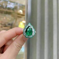 a person holding an emerald and diamond ring