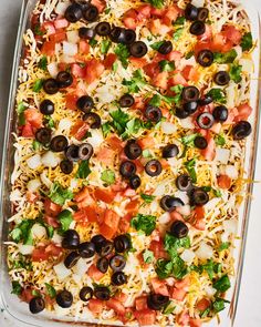 a casserole dish filled with cheese, olives, tomatoes and other toppings