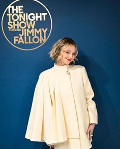 a woman standing in front of a blue wall with the tonight show logo on it