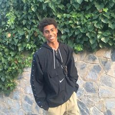 a young man standing in front of a stone wall with ivy growing on the side