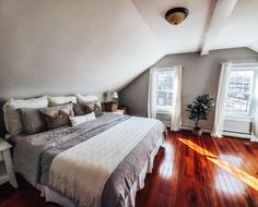 a large bed sitting in the middle of a bedroom next to two windows on top of a wooden floor