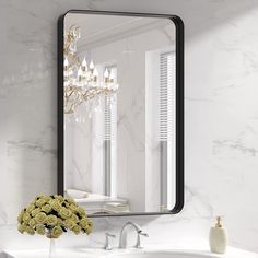 a white sink sitting under a large mirror next to a vase with flowers in it