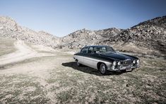 an old car is parked on the side of a dirt road