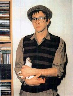 a man holding a cat in his arms while standing next to a book shelf filled with books