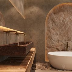 a large white bath tub sitting next to two sinks in front of a stone wall