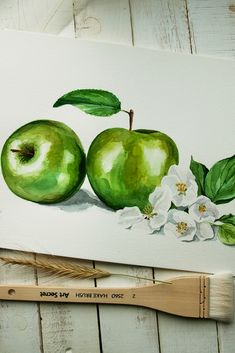 two green apples with leaves and white flowers on a piece of paper next to a paintbrush