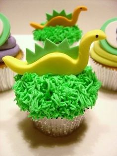 cupcakes decorated with green frosting and yellow icing in the shape of dinosaurs