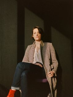 a woman sitting on top of a chair in front of a black wall wearing red boots