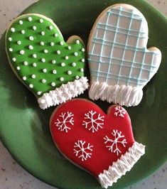 three decorated cookies on a green plate with snowflakes and mittens in the shape of hearts