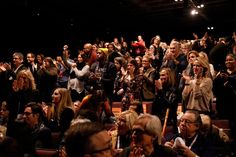 a large group of people are sitting in the auditorium and clapping to someone on their cell phone