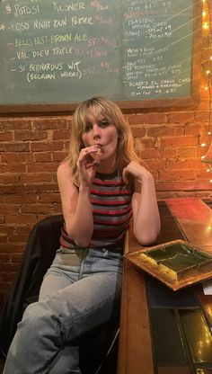 a woman sitting at a table eating food in front of a chalkboard with writing on it