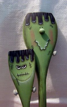 two green ceramic spoons with faces on them sitting next to each other in front of a white wall