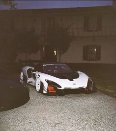 a white and black sports car parked in front of a house at night with the door open