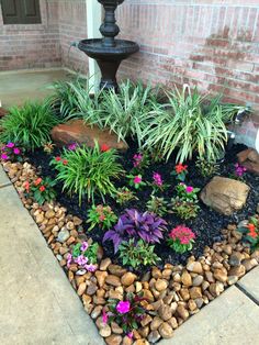 a garden with rocks and flowers in front of a brick building