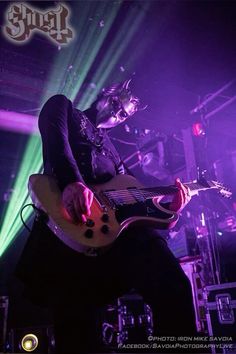 a man playing guitar on stage with purple lighting behind him and green light coming from the ceiling