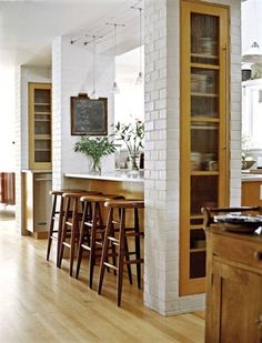 a kitchen with white brick walls and wooden floors, along with bar stools that match the hardwood flooring